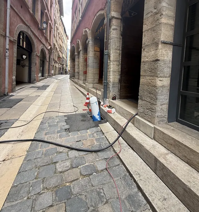 Rue pavée du Vieux Lyon : un flexible court jusqu’à un regard ouvert, d’où sort une gaine de chemisage