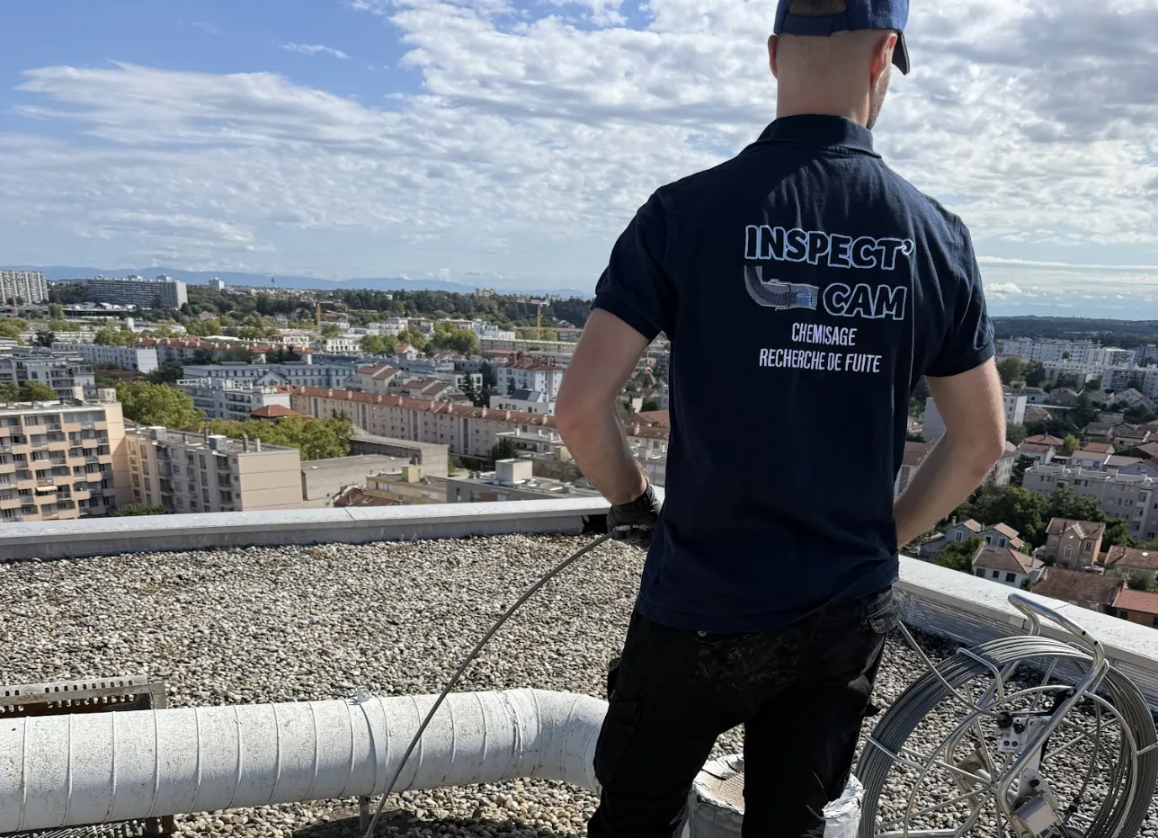 Technicien d’Inspect’ Cam, de dos, en intervention sur un toit-terrasse qui domine la ville