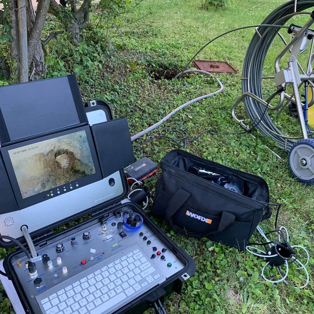 Poste de contrôle d’une caméra d’inspection posé dans l’herbe, près d’un regard ouvert